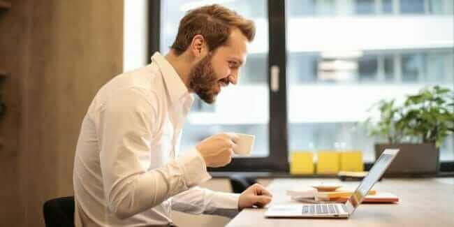 man-holding-teacup-infront-of-laptop-on-top-of-table-inside man-holding-teacup-infront-of-laptop-on-top-of-table-inside